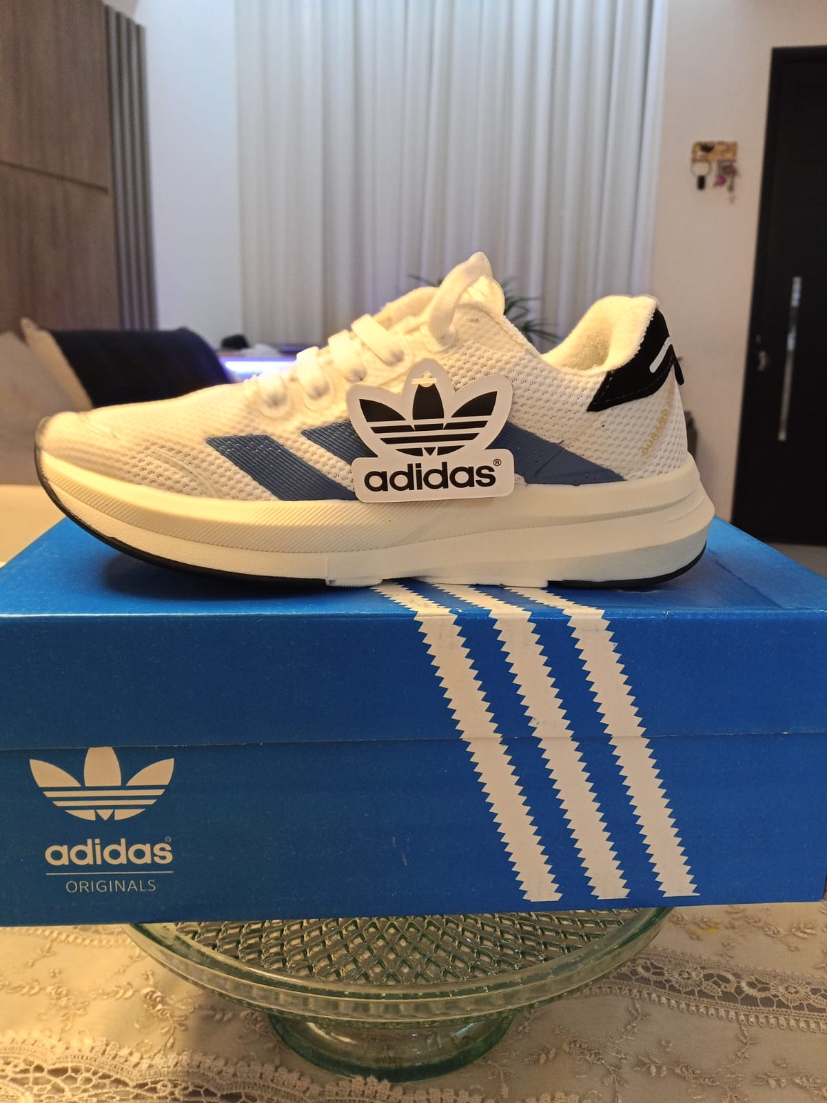 Tênis Adidas branco com listras azuis sobre a caixa azul