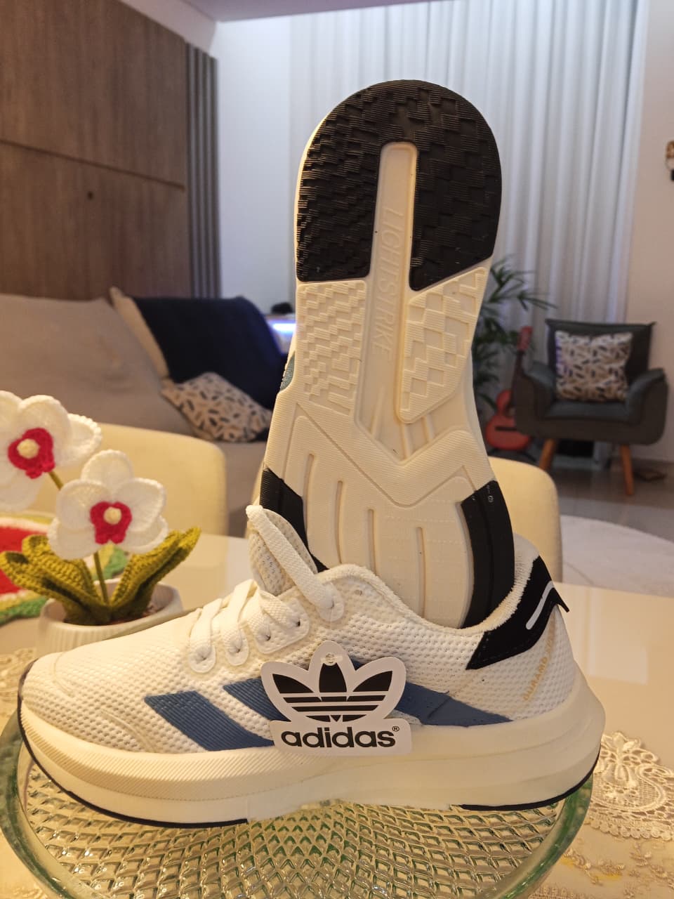 Tênis Adidas branco com listras azuis e solado em exibição